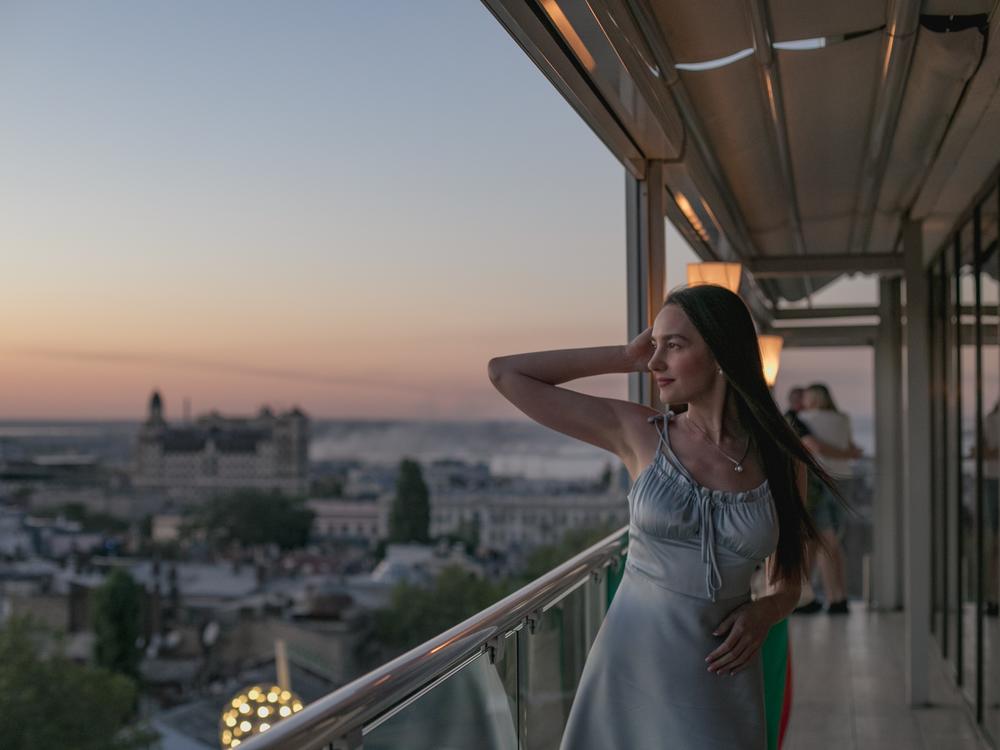 A girl poses for a photo in a restaurant overlooking Odesa on Aug. 14, where smoke from a shelling that occurred just moments earlier can be seen in the background.