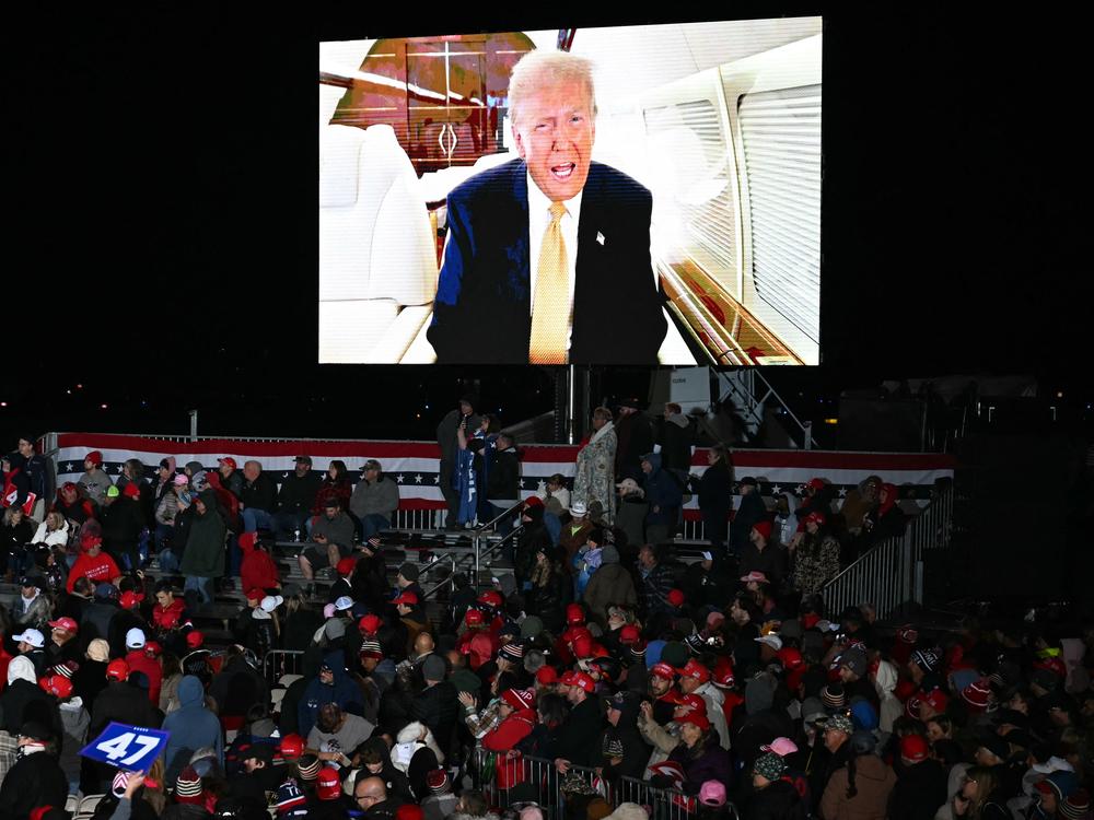 Former President Donald Trump sends a personal message on the jumbotron informing attendees that he would be three hours late for a campaign rally in Traverse City, Michigan, on Friday.