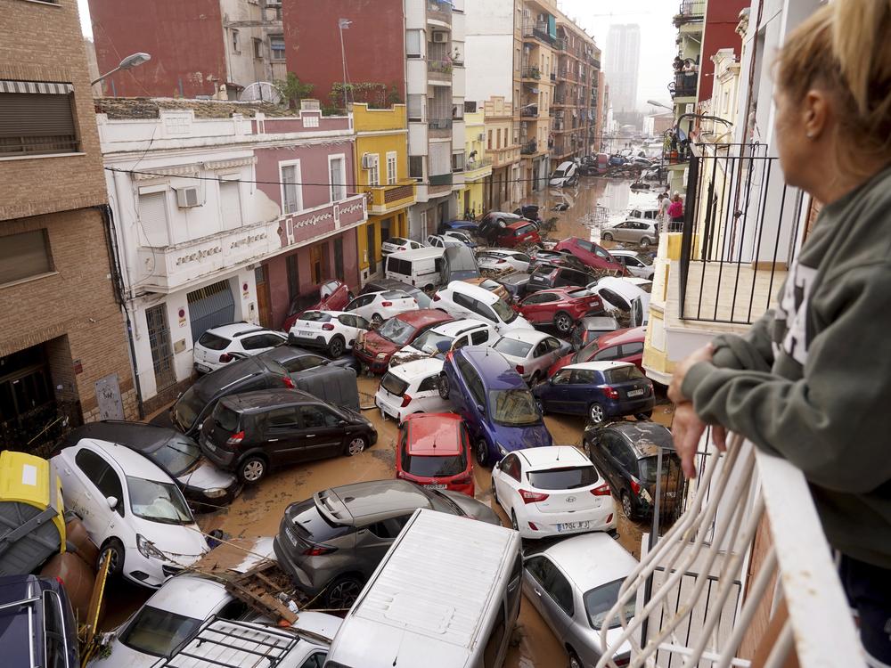 A woman looks out from her balcony as vehicles are trapped in the street during flooding in Valencia.
