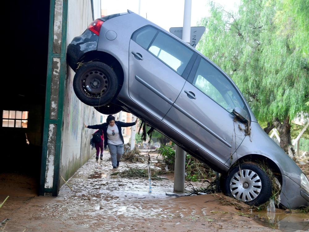 A resident walks next to a car lifted up in a street covered in mud in a flooded area in Picanya, near Valencia.