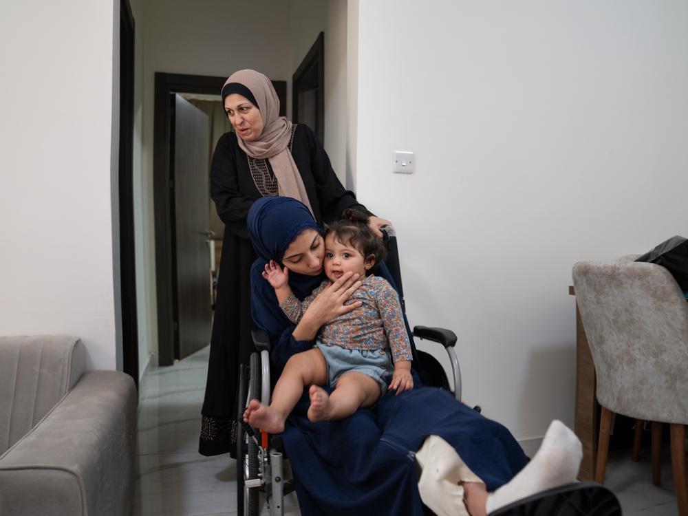 Raneem Hijazi holds her baby, Mariam, on her lap in her wheelchair, as Hijazi's mother-in-law, Soha Sakallah (standing), helps her.