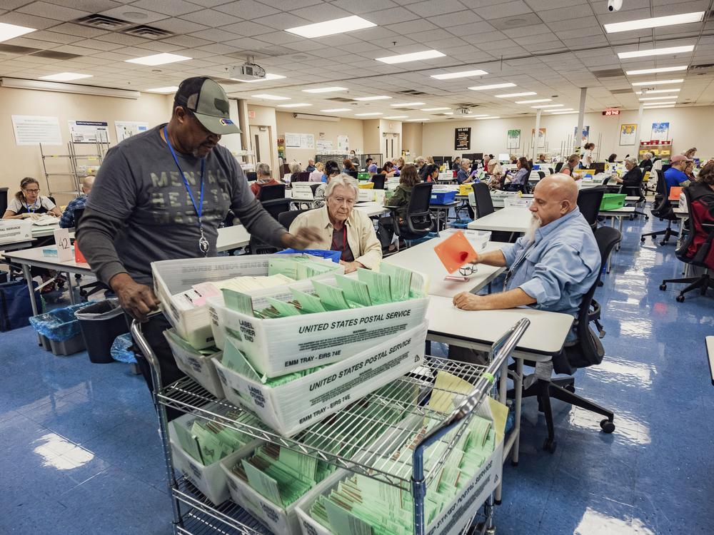 Election workers sort ballots at the Maricopa County Tabulation and Election Center in Phoenix. The workers wear colored lanyards symbolizing their party: red for registered Republicans, yellow for Independents and blue for Democrats. They work in pairs with partners chosen from different political outlooks.