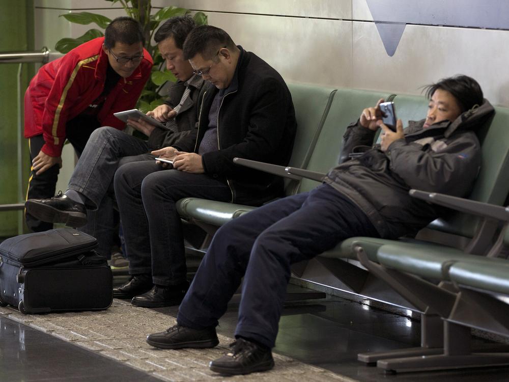 Men browse their tablet computers and smartphone at the Beijing Capital Airport on Nov. 30, 2013.