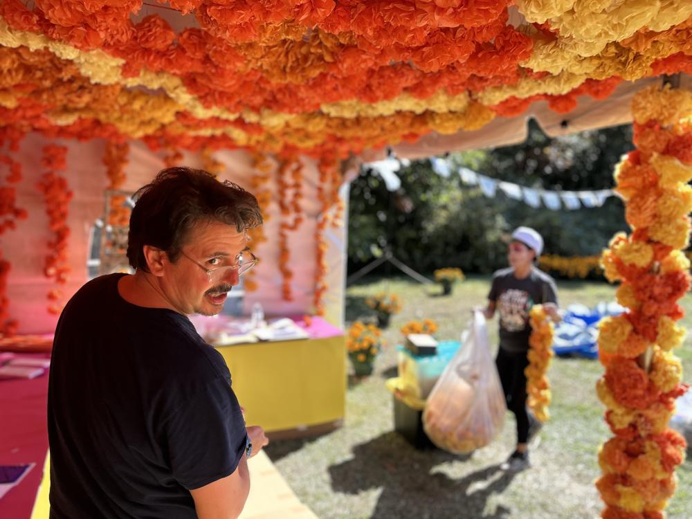 Raleigh artist Peter Marín stands by Día de Oakwood organizer Angela Salamanca under rows of handmade paper flowers as the central public ofrenda is in progress at the Historic Oakwood Cemetery.<br>