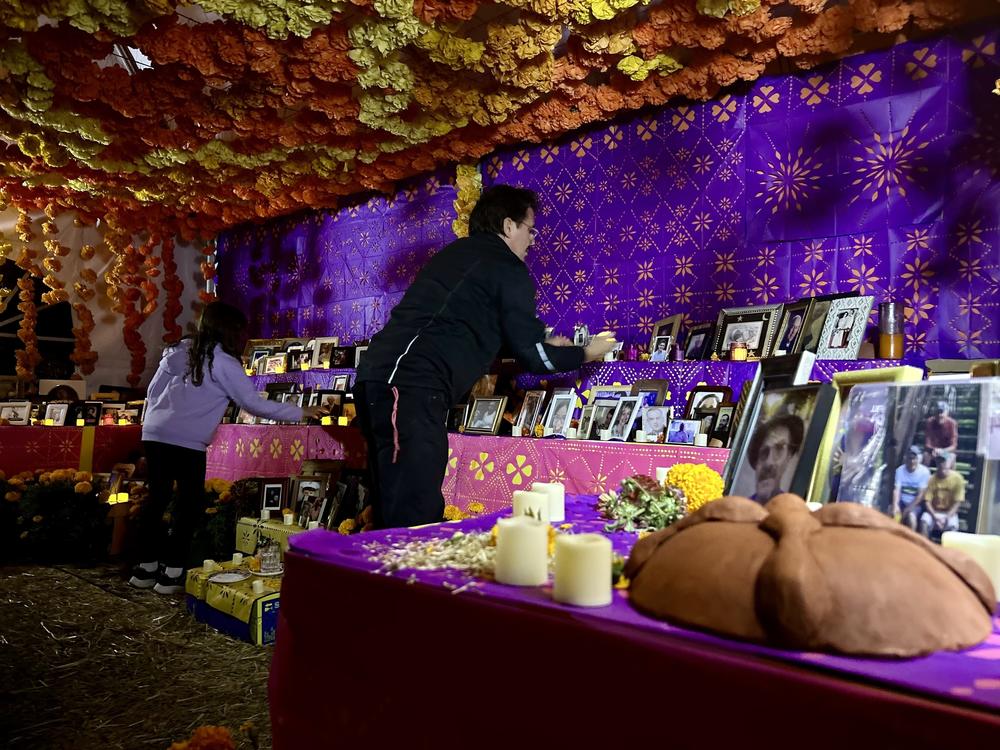 Peter Marín and his daughter Lucía put out candles lit for deceased loved ones at a community ofrenda at the Historic Oakwood Cemetery.<br>