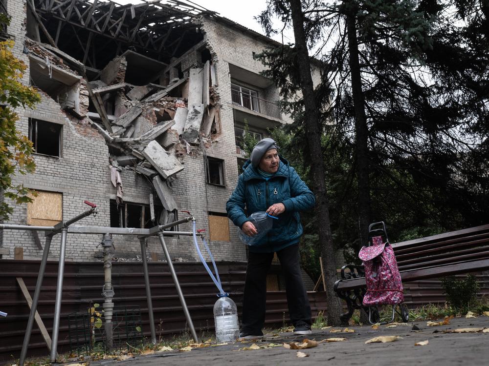 A woman fills bottles with water from a public spigot in front of a bombed out student dormitory in Dobropillya, Ukraine, on Oct. 17.