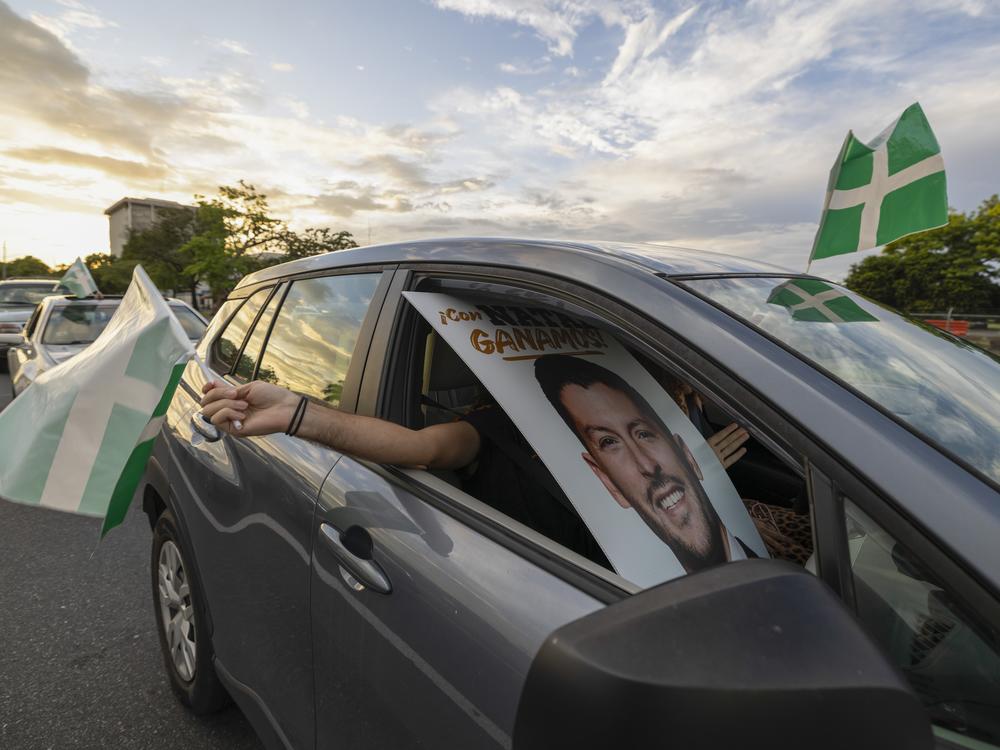 A supporter waves a Puerto Rican Independence Party flag while holding a campaign poster promoting the Citizens' Victory Movement mayoral candidate Manuel Natal, during a caravan in San Juan, Puerto Rico, Friday, Nov. 1, 2024.