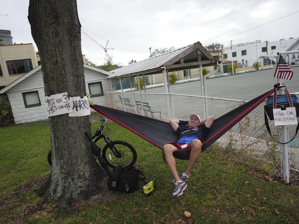 Christopher Reid, 54, a U.S. Army veteran, relaxes in a hammock alongside homemade signs supporting Democratic presidential nominee Vice President Kamala Harris and Florida's Amendments 3 and 4, which would legalize recreational marijuana and enshrine abortion rights in the state, respectively, across from a polling place at the Coliseum in downtown St. Petersburg, Florida on Tuesday.