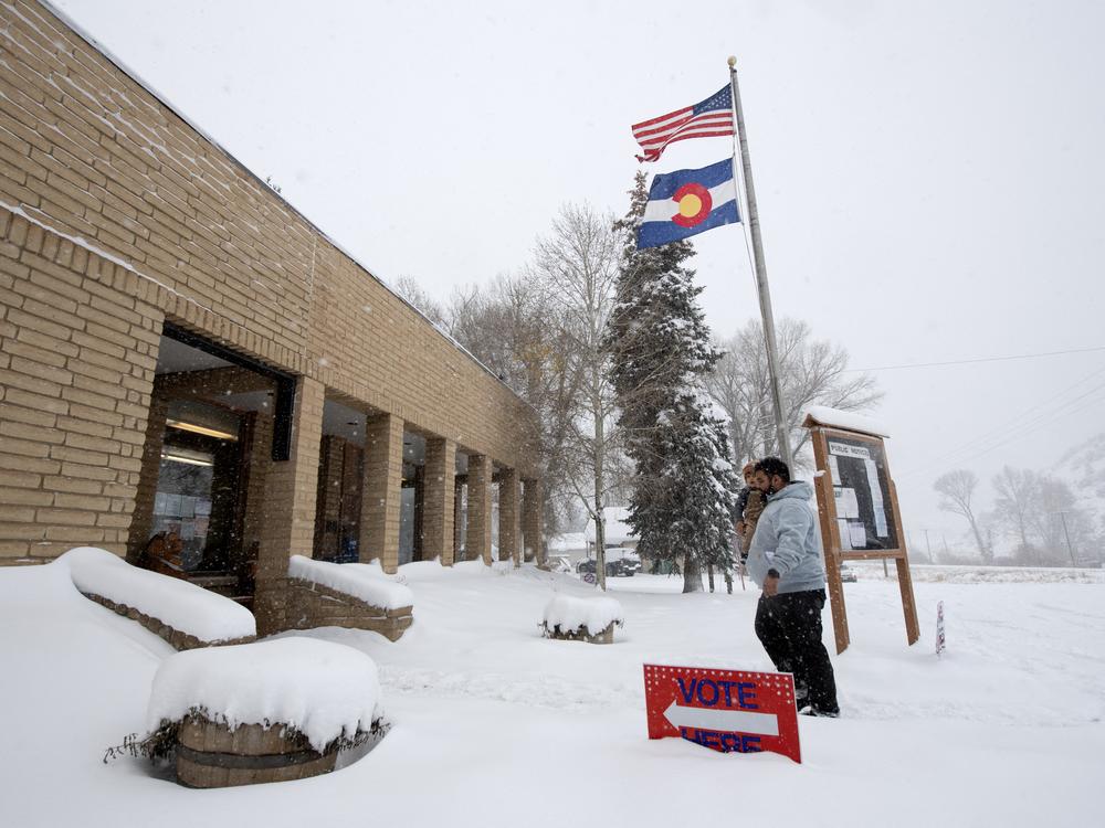 Cristian Ortega carries his son Luca as he walks in the snow into the Oak Creek Town Hall to drop off his ballot on Election Day, November 5, 2024, in Oak Creek, Colorado.