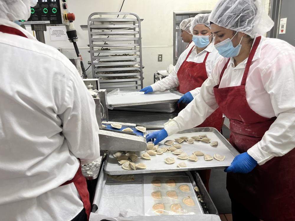 The empanada maker machine at MasPanadas produces about 5,000 pounds of empanadas a day. Staffers arrange them in trays to be taken to the fryer.