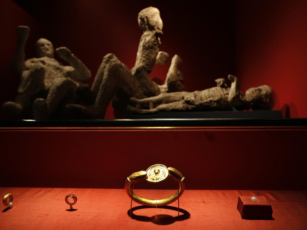 Jewelry found in the ruins of a house in Pompeii are displayed, backdropped by the casts of two adults and two children who died together, are seen housed at the British Museum in London in 2013.