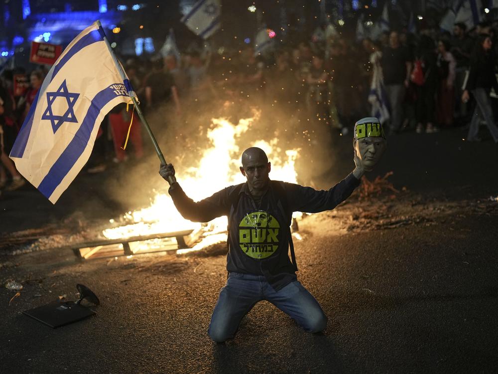 A protester holds an Israeli flag as Israelis light a bonfire during a protest after Prime Minister Benjamin Netanyahu has dismissed his defense minister Yoav Gallant in a surprise announcement in Tel Aviv, Israel, Tuesday, Nov. 5, 2024.