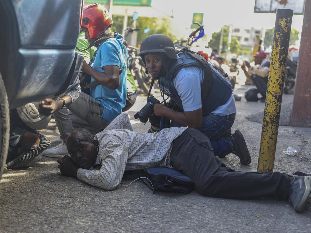 Journalists take cover from the exchange of gunfire between gangs and police in Port-au-Prince, Haiti, Monday.
