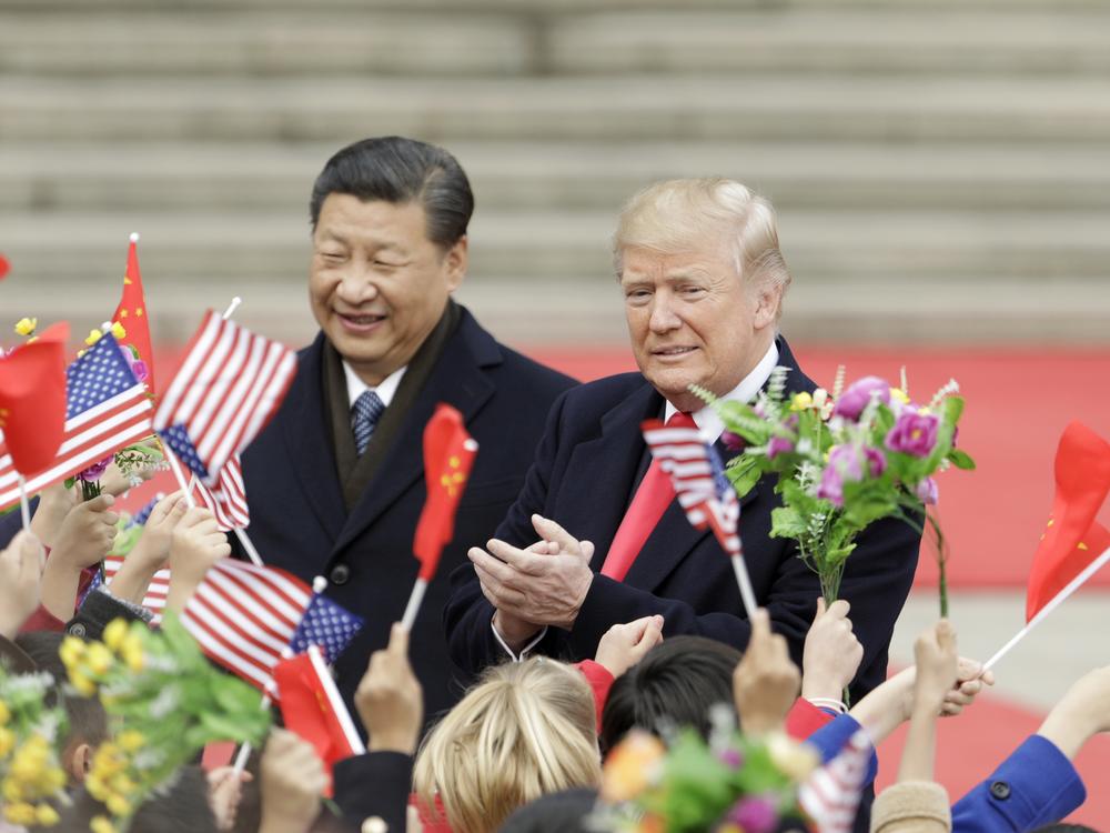 President Donald Trump, right, and Xi Jinping, China's president, greet attendees waving American and Chinese national flags during a welcome ceremony outside the Great Hall of the People in Beijing, China, on November 9, 2017. 2017.