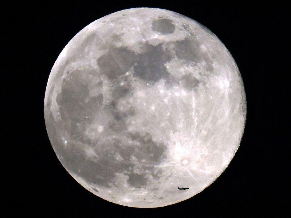 A commercial airliner flies before the rising Beaver full moon above Kuwait City on Nov. 27, 2023.
