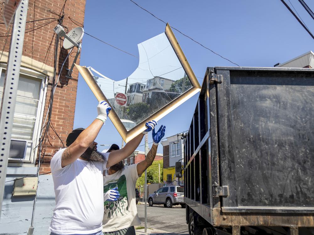 A local resident helps outreach worker Thomas Bradley (right) during a cleanup event in Philadelphia's Kensington neighborhood on Sept. 3, 2024.  Bradley works with Ride Free, a local nonprofit focused on gun violence and neighborhood resilience.