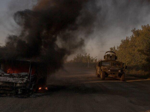 A Ukraine's Humvee armored military vehicle drives past a burning car on a road near the border with Russia, in the Sumy region of Ukraine, on August 14.