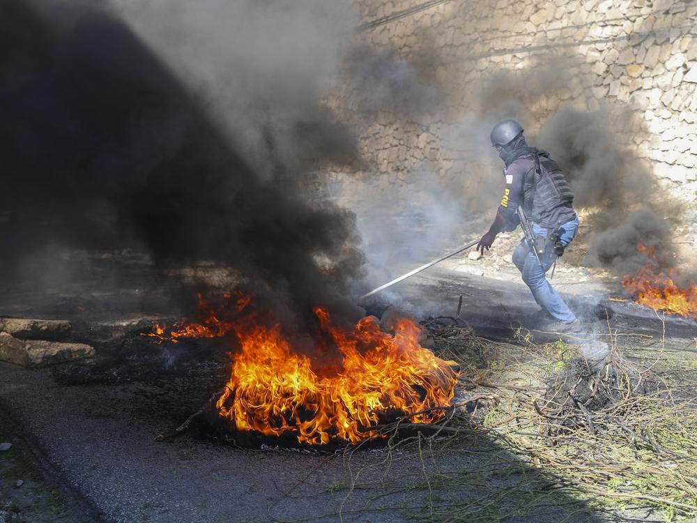 A police officer works to clear barricades of burning tires set on fire by residents to deter gang members from entering their neighborhood, in Port-au-Prince, Haiti on Tuesday.
