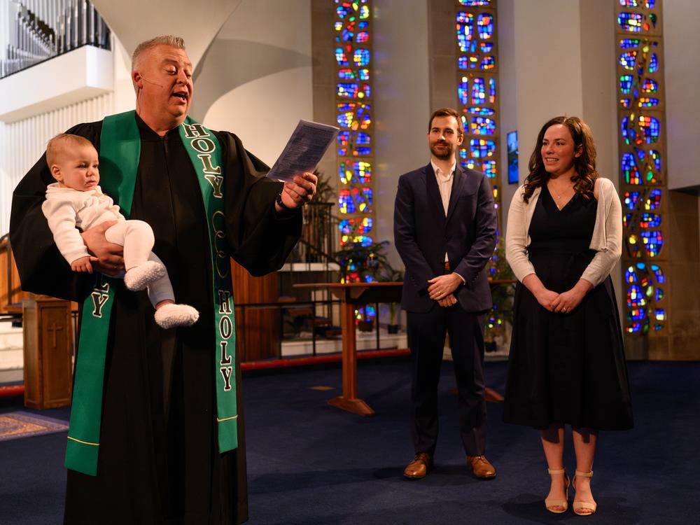 Pastor Chris Morgan — parishioners call him Pastor Chris — holds 8-month-old Elliott Holdren after his baptism, as his mother, Megan Holdren, and father, Matt Holdren, look on during a traditional service at Christ United Methodist Church.
