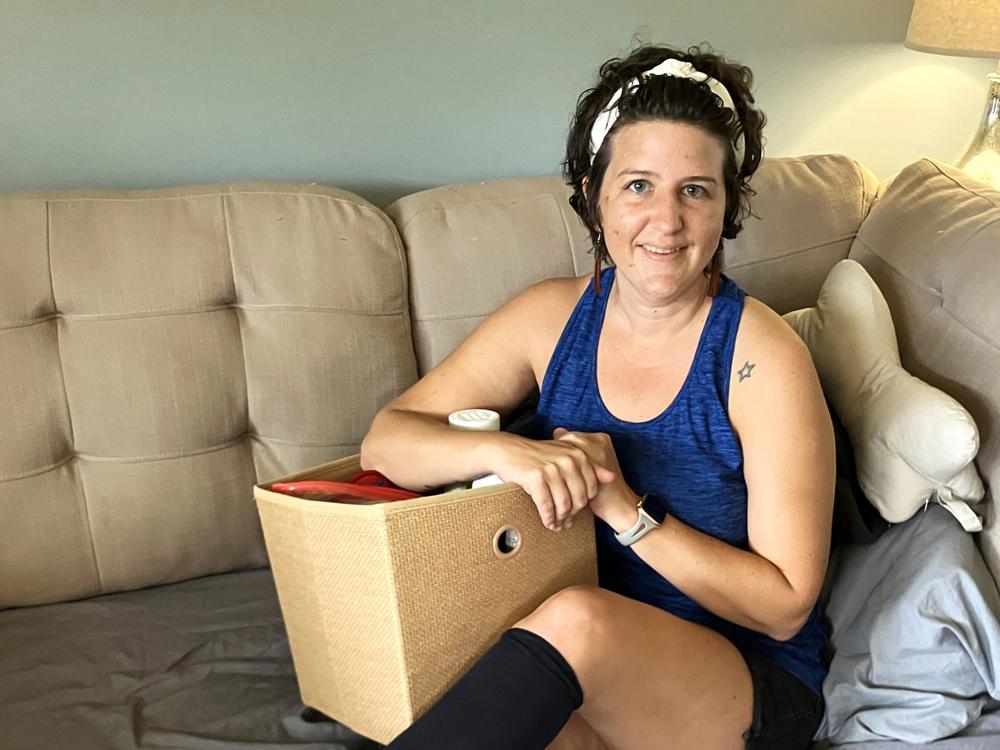 Erica Hayes, 40, sits on her sofa with a box where she keeps the medical supplies she needs to manage her long COVID symptoms, which include chronic fatigue, irregular heart rate, low blood pressure, hives, migraines and internal tremors.