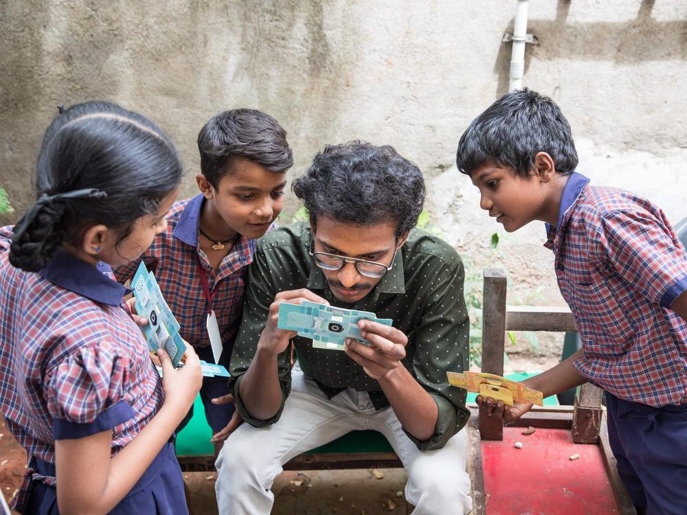 A.Santhos inserts a slide into the foldscope. He is a former student who lives in the neigbourhood and keeps in touch with the students of his alma mater, often taking them for nature walks to examine the world around them through the foldscope.