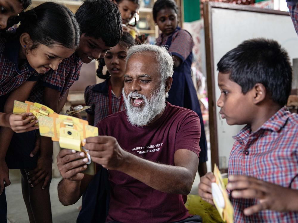 Mo Pandiarajan, founder of Eden school, shows students a view of a specimen in a Foldscope, which he's attached to his mobile phone.