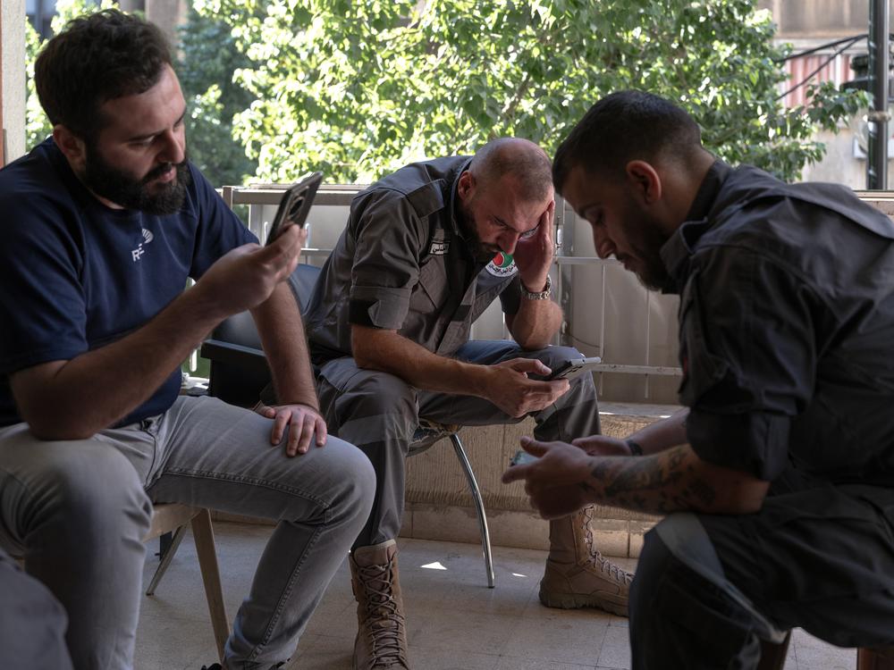 Search-and-rescue volunteers of the Lebanese Popular Relief Association sit on the balcony of their office and check the news on their phones in Beirut.