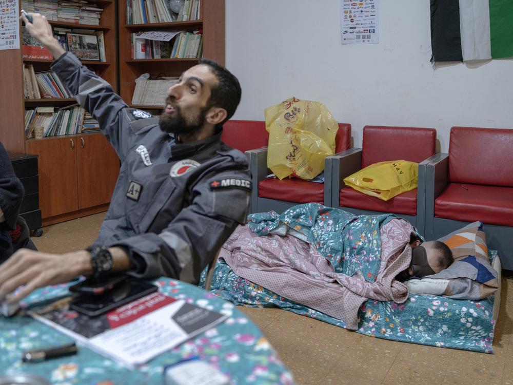 A volunteer gestures at colleagues while another volunteer sleeps behind him. Many  sleep at the emergency center, where they are on call day and night. They have had to flee their homes in areas where Israel carried out its heaviest bombardments.