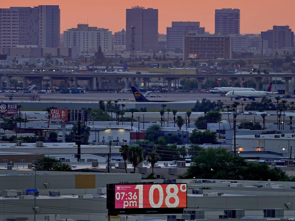 A sign displays an unofficial temperature as jets taxi at Sky Harbor International Airport at dusk, July 12, 2023, in Phoenix.