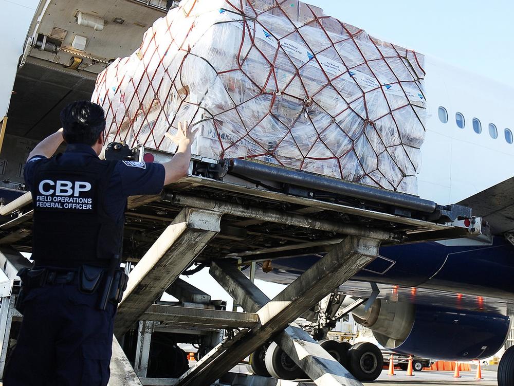 U.S. Customs and Border Protection says it processes some 4 million de minimis shipments every day. Here, CBP officers watch as international shipments are lowered from a plane at Los Angeles International Airport.