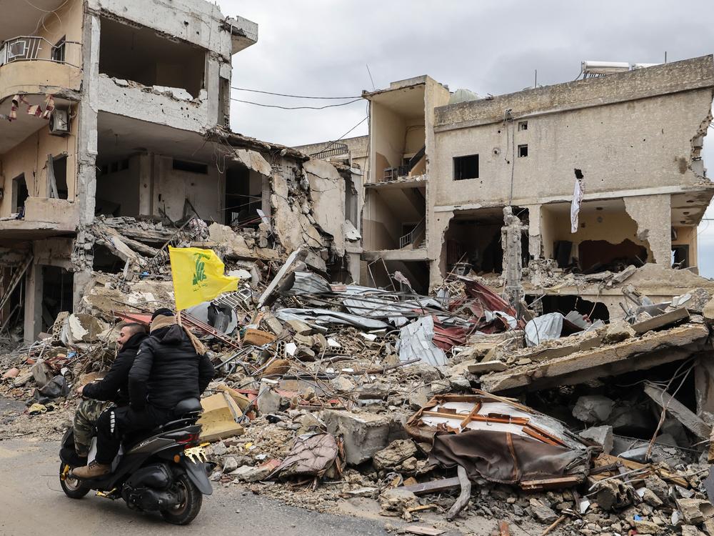 Men ride past destroyed buildings in the southern Lebanese town of Qana as people make their way back to their homes after a ceasefire between Israel and Hezbollah took effect, Wednesday.