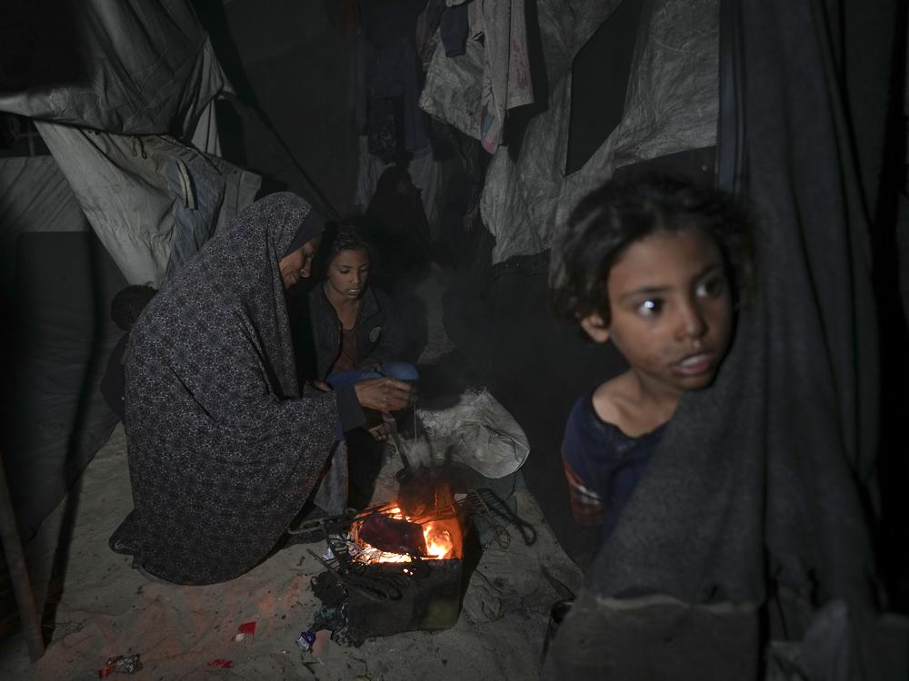 Shireen Daifallah, who was displaced with her children from northern Gaza, checks the fire next to their tent at a camp for displaced people in Deir al-Balah. Gaza Strip, Saturday, Nov. 30, 2024.