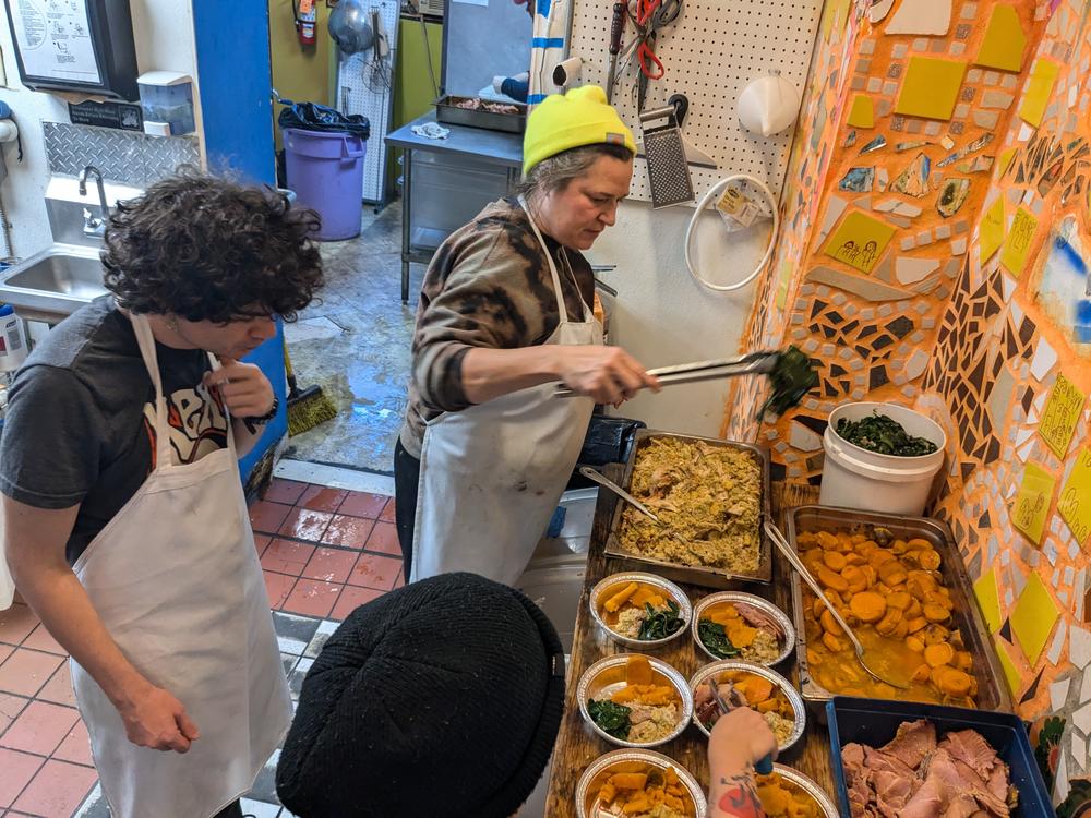 People's Kitchen chef and board member April McGreger instructs volunteers Sam Robbins and Chen Lu on how to put together the day's meal in a to-go container.