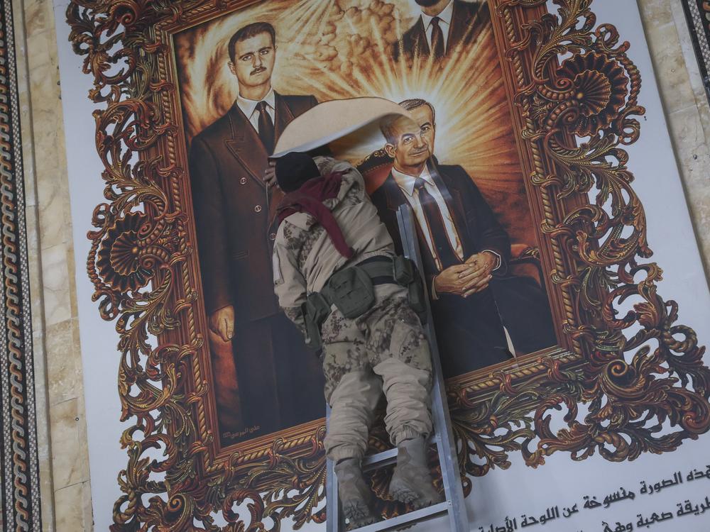 A Syrian opposition fighter tears up a painting Monday depicting Assad and his late father Hazef Assad at the airport in Aleppo, the country's ssecond largest city.