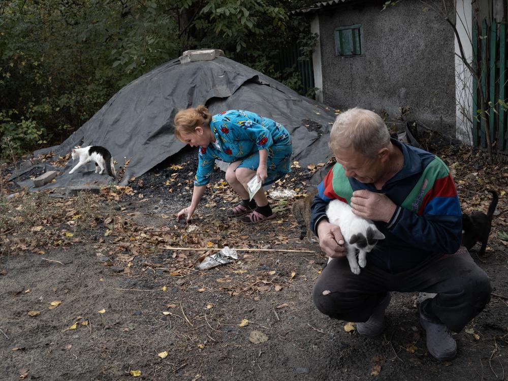Daria Kuznetsova picks through a coal pile while her husband, Voldymyr Kuznetsov, holds one of their cats outside their home in Dobropillya, Ukraine, on Oct. 17. Kuznetsova complains that the coal she has received this season is of poor quality and full of stones.