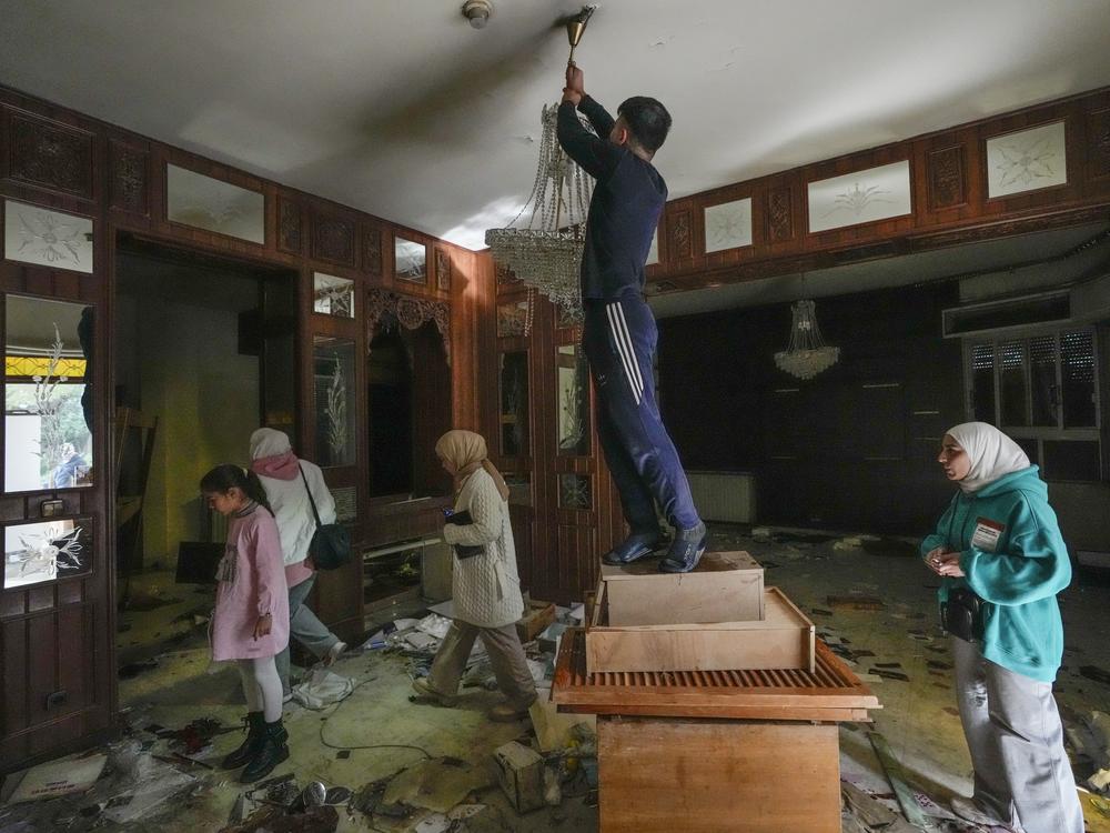 A man tries to take a lamp as people search for belongings in the ransacked private residence of Syrian President Bashar Assad in the Malkeh district of Damascus, Syria, on Sunday.