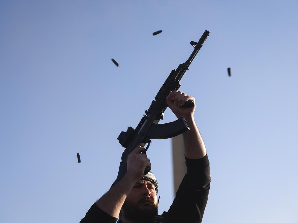 An opposition fighter fires his AK-47 in the air in celebration after opposition forces took control of the city in Damascus.