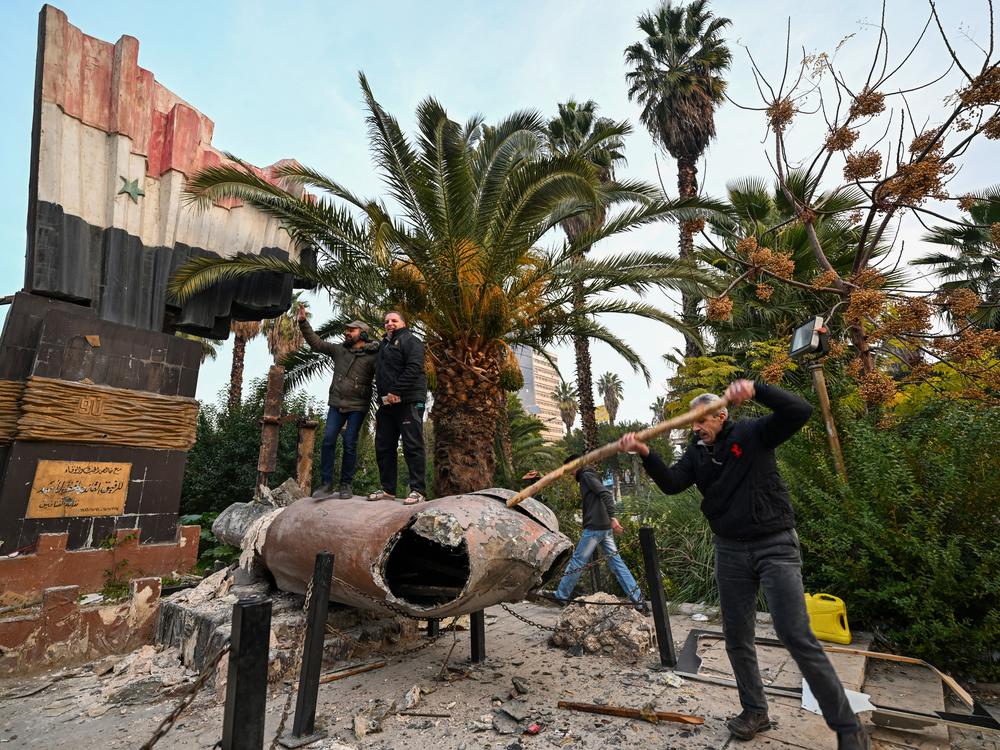 People stand atop a toppled statue of Syria's late president Hafez al-Assad in Damascus.