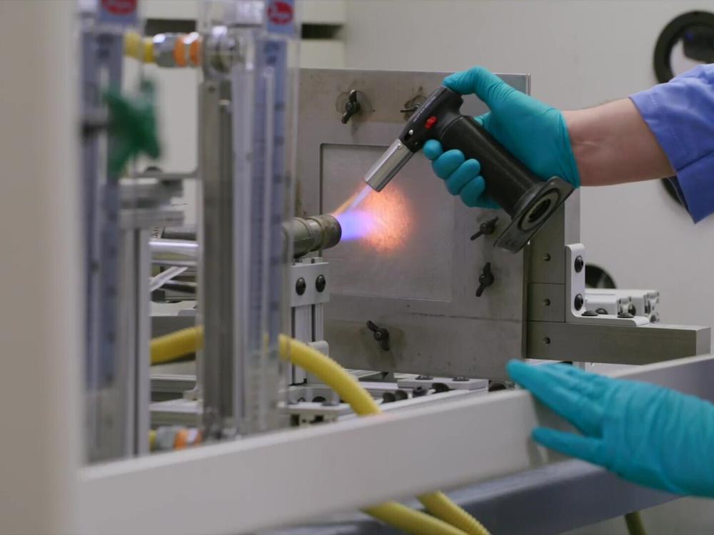 Engineer Matt Gwin puts a piece of aerogel material inside a metal frame and ignites it. After a minute or two, the material is intact and only feels warm.
