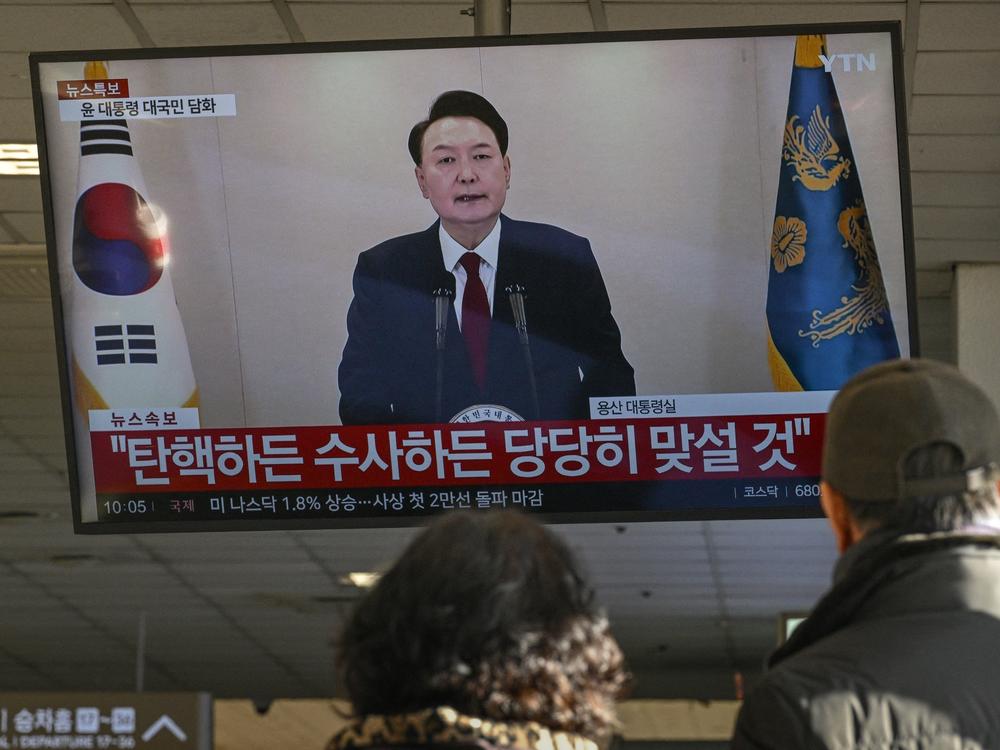 People watch a screen showing South Korean President Yoon Suk Yeol speaking during a televised address at a bus terminal in Seoul on Dec. 12, 2024.