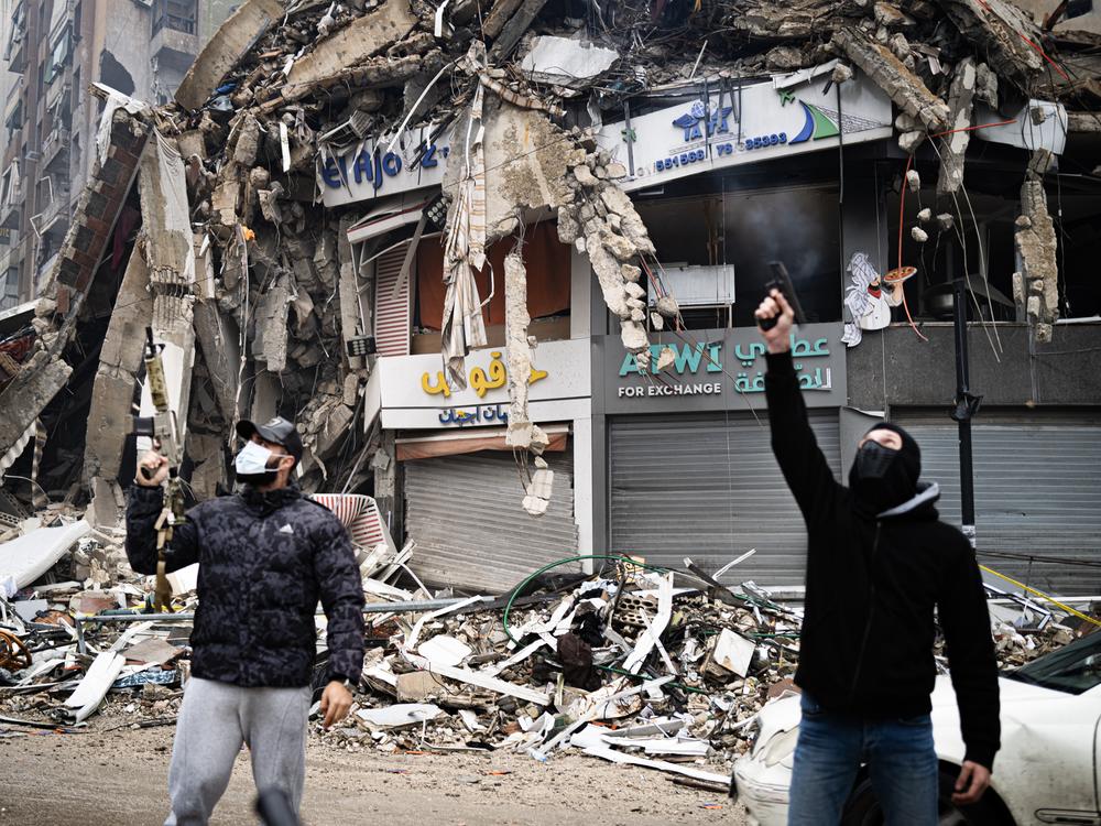 Two masked men fire celebratory shots into the air in Dahiyeh, a Hezbollah stronghold in the southern suburbs of Beirut, which has been devastated by the recent war with Israel.