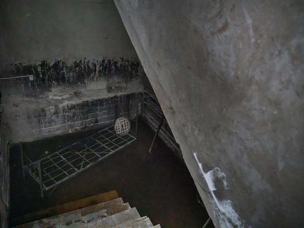 A bed frame sits in a dark room with a brown liquid covering the floor. Moustafa says its a pit of acid where detainees were thrown to die.