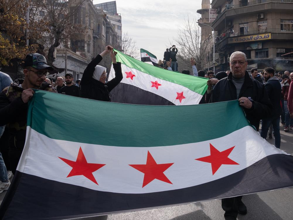 People hold the new Syrian flag during the funeral procession for Syrian activist Mazen al-Hamada.