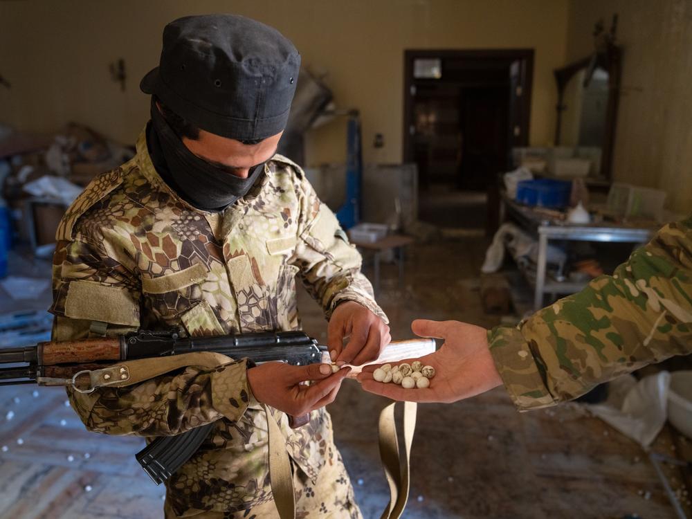 A soldier with the HTS shows how Captagon pills fit into the pill holders scattered across the floor.