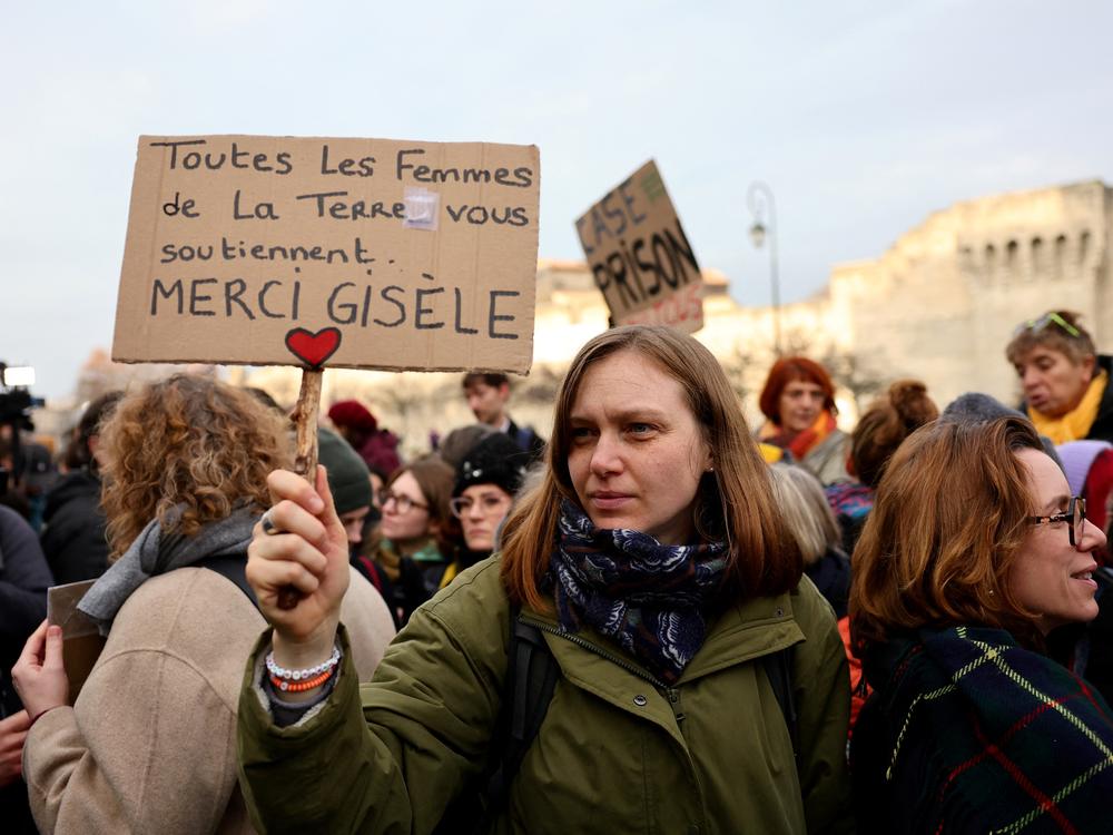 A woman holds a placard reading in French 