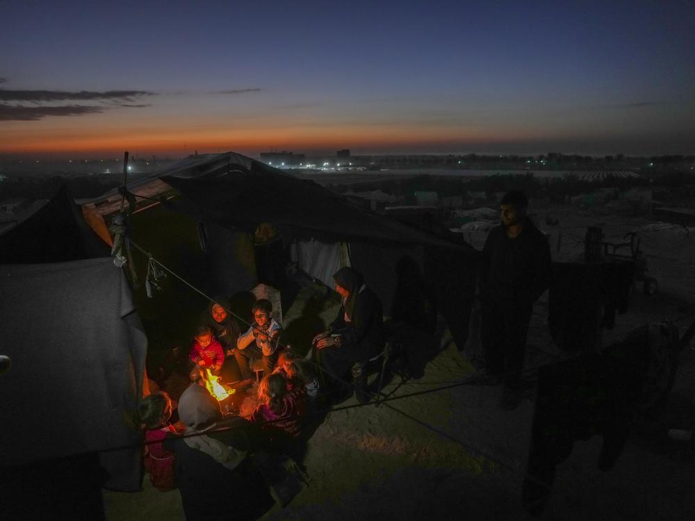 Reda Abu Zarada, 50, displaced from Jabaliya in nothern Gaza, sits by a fire with her grandchildren at a camp by the sea in Khan Younis, Gaza Strip, Thursday, Dec. 19, 2024.