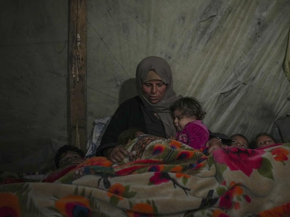 Reda Abu Zarada wraps herself and her grandchildren in blankets as they prepare to sleep in their tent at a camp in Khan Younis, Gaza Strip, Thursday Dec. 19, 2024.