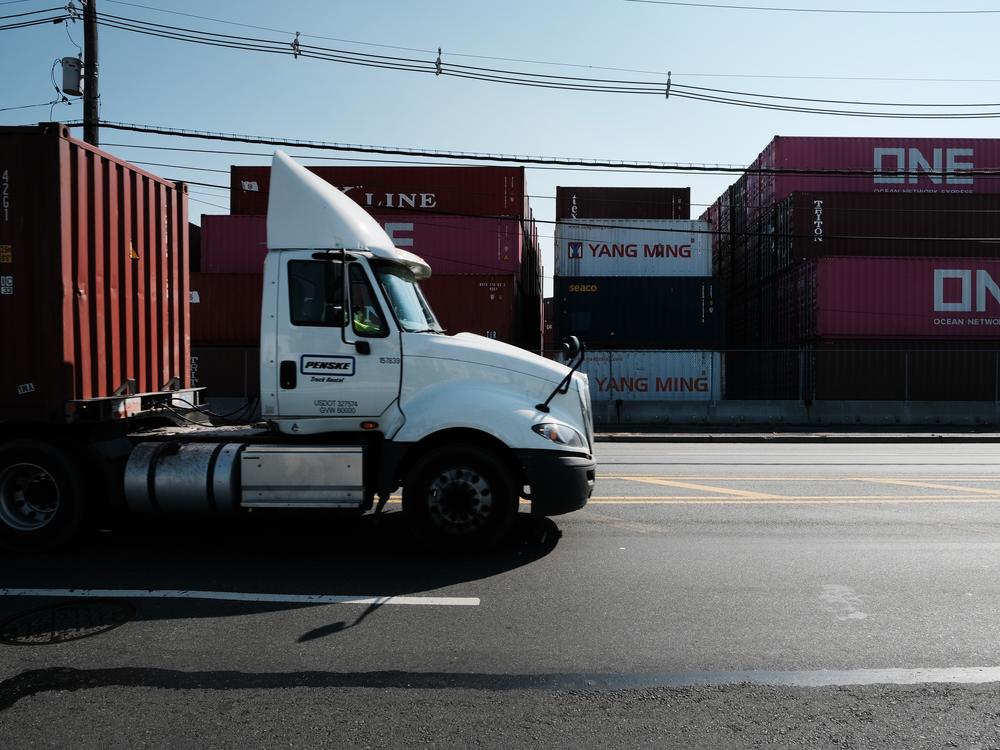 Trucks move past cargo containers at a port in Bayonne, N.J., in 2021. The state is adopting California's Advanced Clean Trucks rules, which require at least 7% of medium- and heavy-duty vehicles sold in the state to be zero-emission for model year 2025. Dealers are petitioning for a delay, so far unsuccessfully.