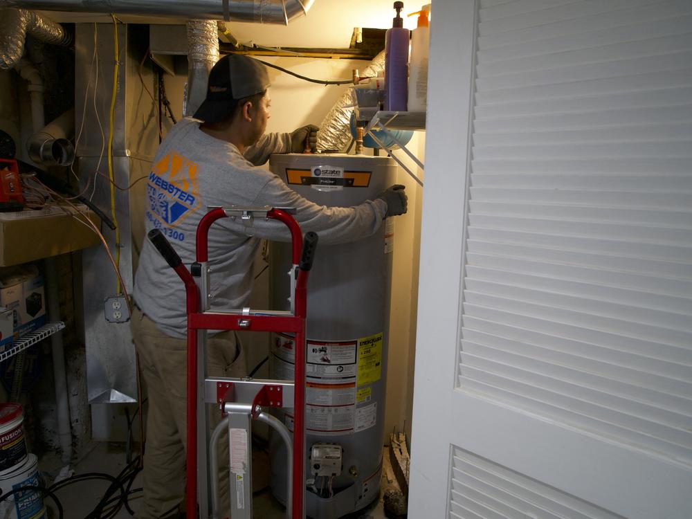 A technician removes a gas water heater from a home in Washington, DC. Researchers see heat pumps as climate solutions because they often replace appliances that run on fossil fuels like gas. Heat pumps run on electricity that's increasingly powered by renewable energy.