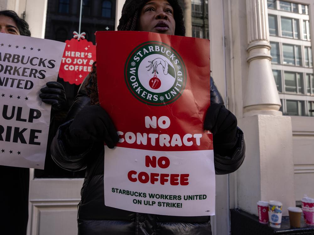 People hold signs outside of a closed Starbucks as employees strike on Monday in New York City.